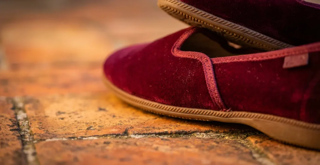 Dettaglio macro di friulane in velluto color borgogna su pavimento in legno